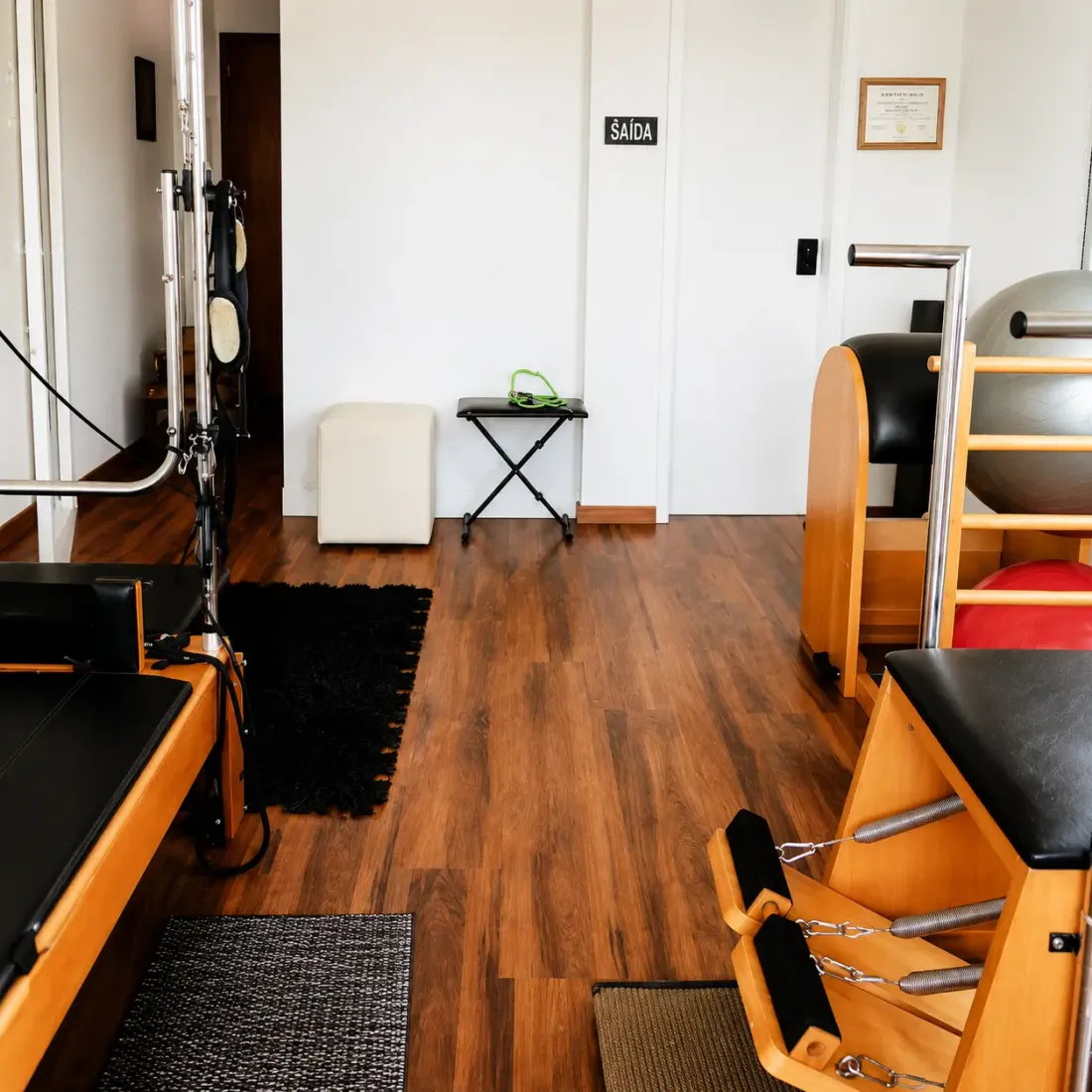 Estúdio de Pilates terapêutico com reformer, chair e barril sobre piso de madeira
