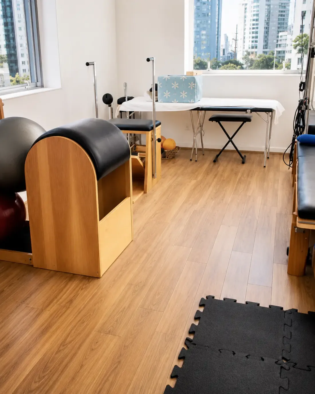 Sala do consultório com maca, barril de Pilates e janela ampla com vista para os prédios de São Paulo